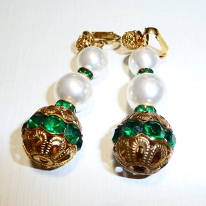 May include: A pair of gold tone clip-on earrings with three white faux pearl beads and a large green crystal ball at the bottom.