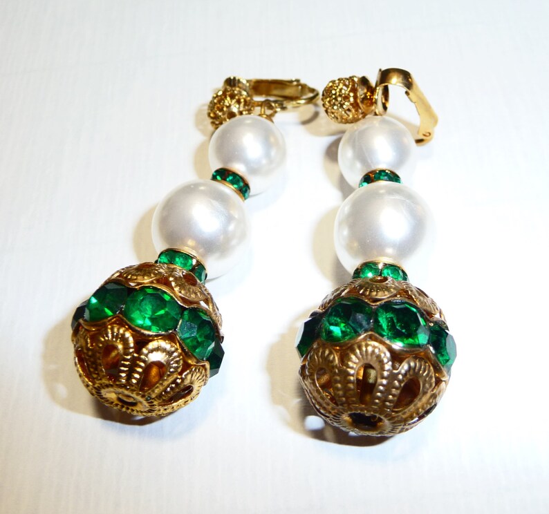 May include: A pair of gold tone clip-on earrings with three white faux pearl beads and a large green crystal ball at the bottom.