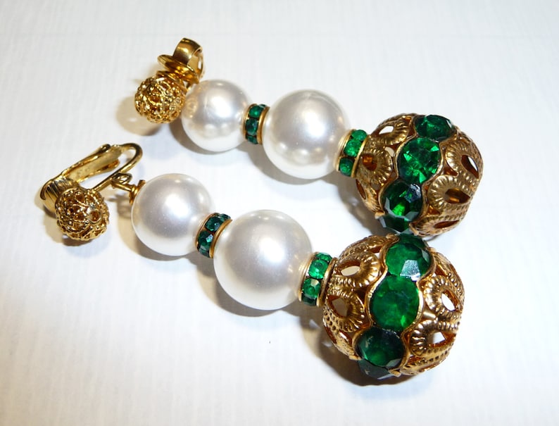 May include: Gold tone clip-on earrings with two white pearl beads and a green rhinestone ball.