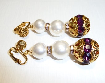 May include: A pair of gold tone clip-on earrings with purple and clear rhinestones and white faux pearls.