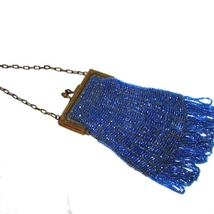 May include: A small, vibrant blue beaded handbag featuring a metallic frame with a kiss-lock closure and a thin, dark metal chain strap. The body of the bag is covered in intricate blue glass beads, finished with a long, dangling beaded fringe.