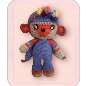 Puede incluir: Juguete de amigurumi de crochet de oso pixie de flores, con una combinación de colores púrpura, naranja y azul. El oso tiene una corona de flores con flores de colores. El juguete está de pie sobre un fondo rosa.