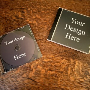 May include: Two blank CD cases, one with a clear plastic cover and the other with a black cover. Both cases have the text "Your Design Here" printed on them.