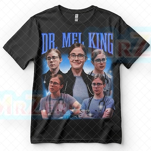 May include: Black t-shirt with a collage of images of a woman wearing glasses and a stethoscope. The text "DR. MEL KING" is printed in blue above the images. The images show the woman in various poses, some wearing scrubs.