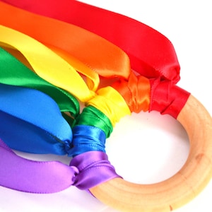 May include: Rainbow ribbon toy with a wooden ring. The ribbons are tied to the ring and are in the colors of the rainbow: red, orange, yellow, green, blue, indigo, and violet.