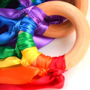 May include: Rainbow ribbon tied around wooden rings. The ribbons are in the colors of the rainbow, red, orange, yellow, green, blue, indigo, and violet.
