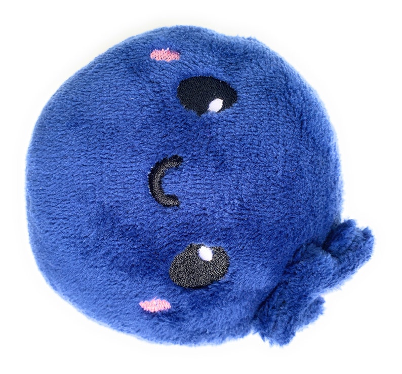 May include: A blue plush toy shaped like a whale with a smiling face. The whale has two black eyes with white highlights and a pink blush on each cheek.