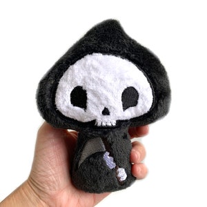 May include: A plush black and white Grim Reaper toy with a skull face and a scythe. The toy is about 15 cm tall and is made of soft, fuzzy fabric.