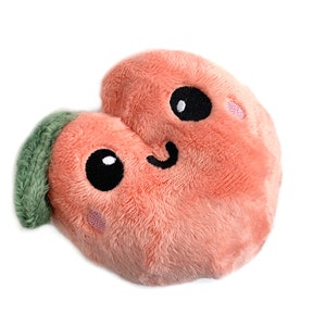 May include: A plush peach-colored heart-shaped toy with a green leaf on top. The toy has a smiling face with black eyes and pink cheeks.