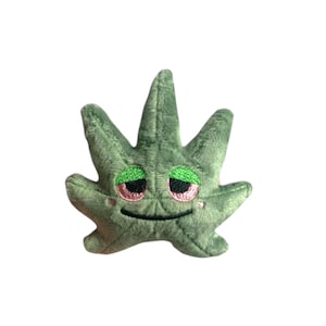 May include: Green plush marijuana leaf with a smiling face and closed eyes. The eyes are green with pink eyelids.