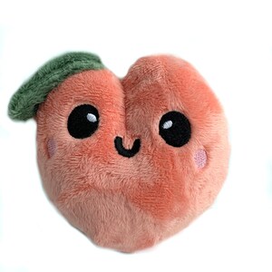 May include: A plush peach-colored peach with a green leaf on top. The peach has a smiling face with black eyes and a black mouth.