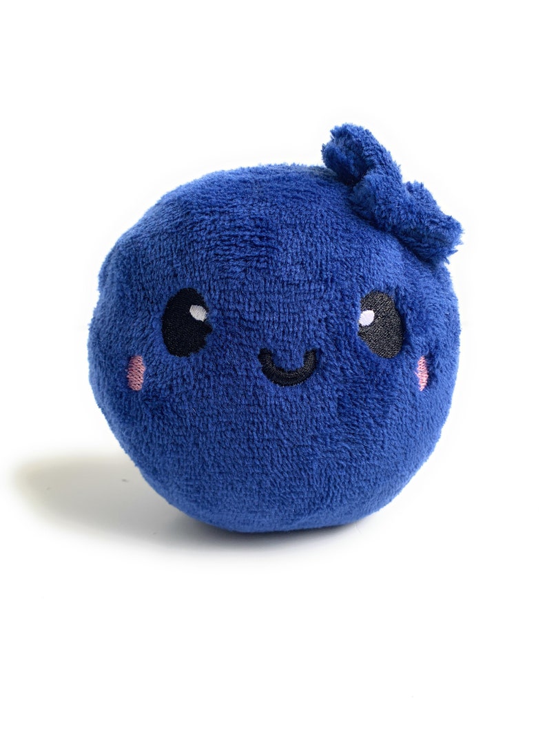 May include: A plush blue blueberry with a happy face, embroidered eyes, and a pink blush. The blueberry has a small, fluffy stem on top.