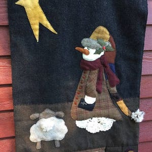 May include: A felt Christmas wall hanging with a snowman, a lamb, and a star. The text on the hanging reads "Said the night wind to the little lamb, 'Do you see what I see?'"