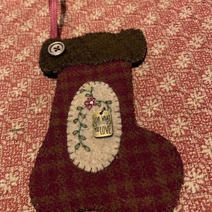 May include: A felt Christmas stocking ornament with a brown cuff and a burgundy body. The stocking has a small embroidered flower and a metal tag that reads "Live what you love".