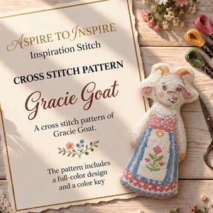 May include: A cross stitch pattern titled Aspire to Inspire Inspiration Stitch Gracie Goat. The document features text and a floral graphic. Beside it lies a finished cross stitch of a goat wearing a blue and pink dress with floral details.