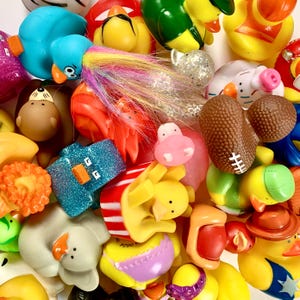 May include: A collection of colorful rubber duck toys in various shapes and sizes. The ducks are made of soft, flexible rubber and feature different designs, including a blue duck with a long, white tail, a yellow duck with a red beak, and a green duck with a red beak. The ducks are arranged in a random order, creating a playful and whimsical scene.