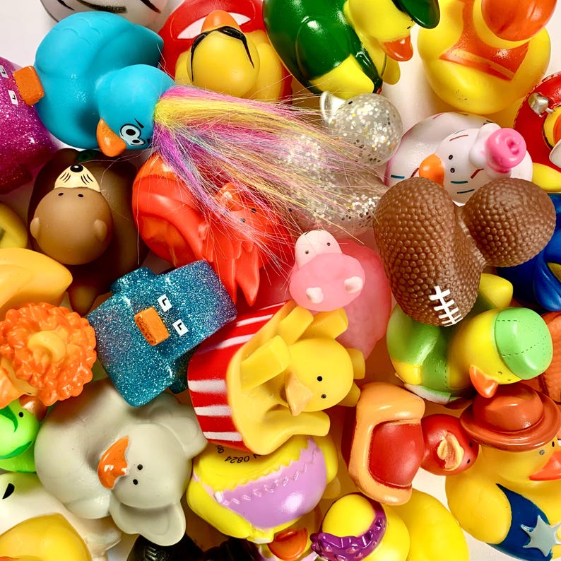 May include: A collection of colorful rubber duck toys in various shapes and sizes. The ducks are made of soft, flexible rubber and feature different designs, including a blue duck with a long, white tail, a yellow duck with a red beak, and a green duck with a red beak. The ducks are arranged in a random order, creating a playful and whimsical scene.