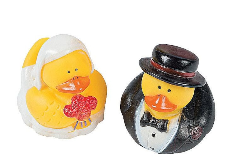 May include: A pair of rubber duck wedding figurines. The bride duck is wearing a white dress and holding a bouquet of red roses. The groom duck is wearing a black tuxedo and a top hat.