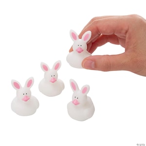 May include: White rubber duckies with bunny ears, pink noses, and pink inner ears. One duck is held by a hand. The other three are scattered on a white background. These Easter-themed bath toys are fun for kids.