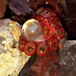 May include: A red, orange, and yellow glass sculpture with a clear glass orb in the center. The sculpture is surrounded by various crystals.