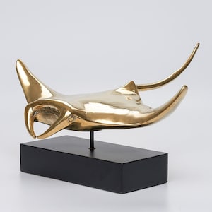 May include: A gold-coloured metal sculpture of a manta ray on a black wooden base.