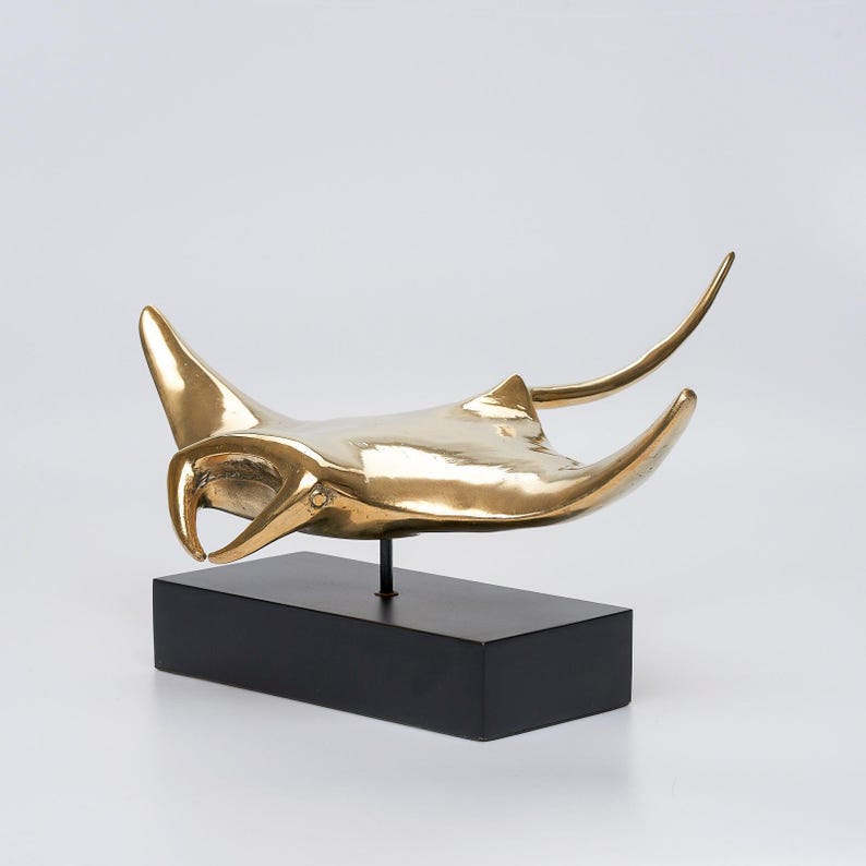 May include: A gold-coloured metal sculpture of a manta ray on a black wooden base.