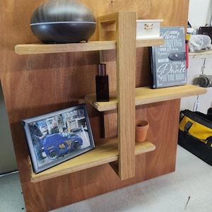 May include: A wooden shelf unit with four shelves. The top shelf has a dark brown diffuser, the second shelf has a small white box and a grey journal with the text "About Waiting for a storm to pass... Dance in the rain", the third shelf has a small bottle, and the bottom shelf has a framed photo of a child in a blue toy car.