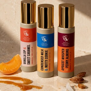 May include: Three perfume bottles with gold caps and colorful labels. The labels read "Vanilla Sip & Sweet Caramel", "Condensed Milk & Nutty Cookie", and "Apricot Whisper & Peony Almond". An apricot slice, caramel drizzle, and almonds are also present.