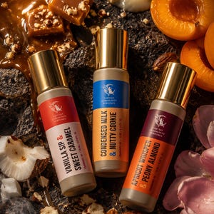 May include: Three perfume bottles with gold caps and colorful labels, featuring the text "Vanilla Sip & Sweet Caramel", "Condensed Milk & Nutty Cookie", and "Apricot Whisper & Peony Almond". The bottles are surrounded by nuts, caramel, and fruit.
