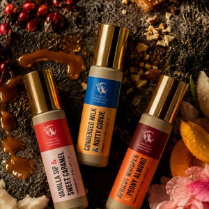 May include: Three fragrance oil bottles with gold caps and labels. The labels read "Vanilla Sip & Sweet Caramel", "Condensed Milk & Nutty Cookie", and "Apricot Whisper & Peony Almond". The bottles are surrounded by nuts, caramel, and fruit.
