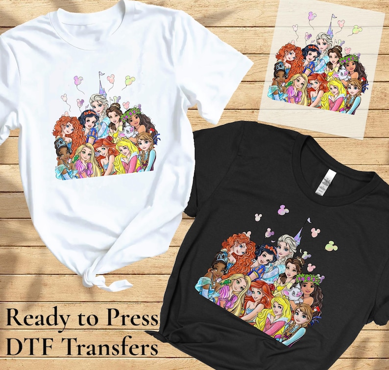 以下が含まれることがあります： 漫画のプリンセスが描かれたカラフルなグラフィックの白と黒のTシャツ。同じプリンセスのグラフィックが描かれた木の板も表示されています。「Ready to Press DTF Transfers」というテキストが画像の下部に印刷されています。