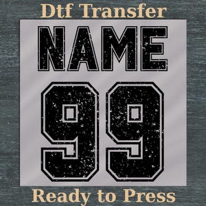 Könnte beinhalten: Ein graues DTF-Transferdesign mit dem Wort "NAME" über der Zahl "99". Der Text "Ready to Press" befindet sich unten. Das Design hat einen Used-Look.