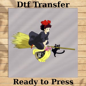 May include: DTF Transfer image featuring a cartoon girl with a red bow riding a broom with a black cat. The girl wears a black dress and is flying over a yellow basket. Text at the top says "Dtf Transfer" and at the bottom "Ready to Press".
