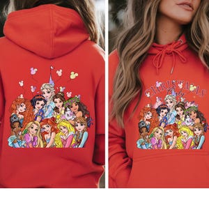 以下が含まれることがあります： ディズニーのプリンセスが描かれた、カラフルなグラフィックの赤いフード付きスウェットシャツ。「Christmas Only」の文字が前面にプリントされています。スウェットシャツの背面には、ディズニーのプリンセスキャラクターとミッキーマウスのアイコンが描かれた同様のデザインがあります。