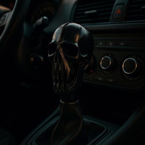 Może przedstawiać: Czarna gałka zmiany biegów w kształcie czaszki. Czaszka ma szczegółowe cechy, w tym oczodoły, jamę nosową i zęby. Gałka jest zamontowana na czarnej dźwigni zmiany biegów w samochodzie.