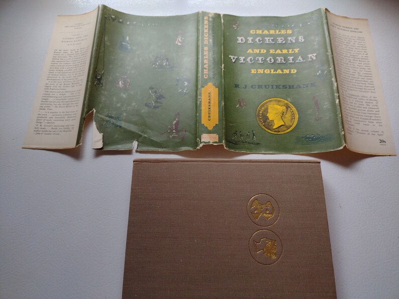 May include: An open book titled "Charles Dickens and Early Victorian England" by R.J. Cruikshank. The cover is green with gold lettering and illustrations. The book is displayed with its pages open, revealing text and illustrations.