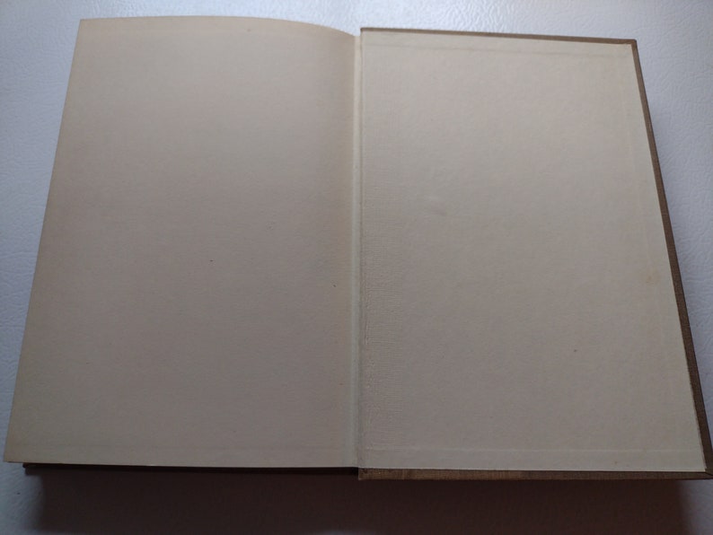 May include: Open book with off-white pages and a brown cover. The pages are blank, and the book is lying open on a surface. The binding is visible, and the edges of the pages are slightly yellowed.