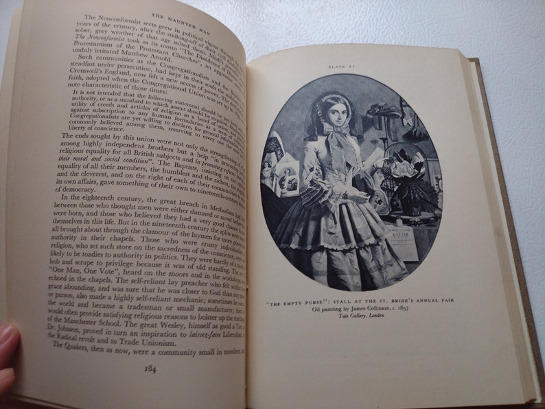 May include: Open book with text and a black and white illustration of a woman in a dress. The illustration is an oil painting titled "The Empty Purse" from 1857. The book is on a light-colored surface.
