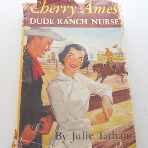 May include: Vintage book cover for "Cherry Ames, Dude Ranch Nurse" by Julie Tatham. The cover features a smiling woman in a nurse's uniform and a cowboy. The background shows a ranch scene with a person riding a horse.
