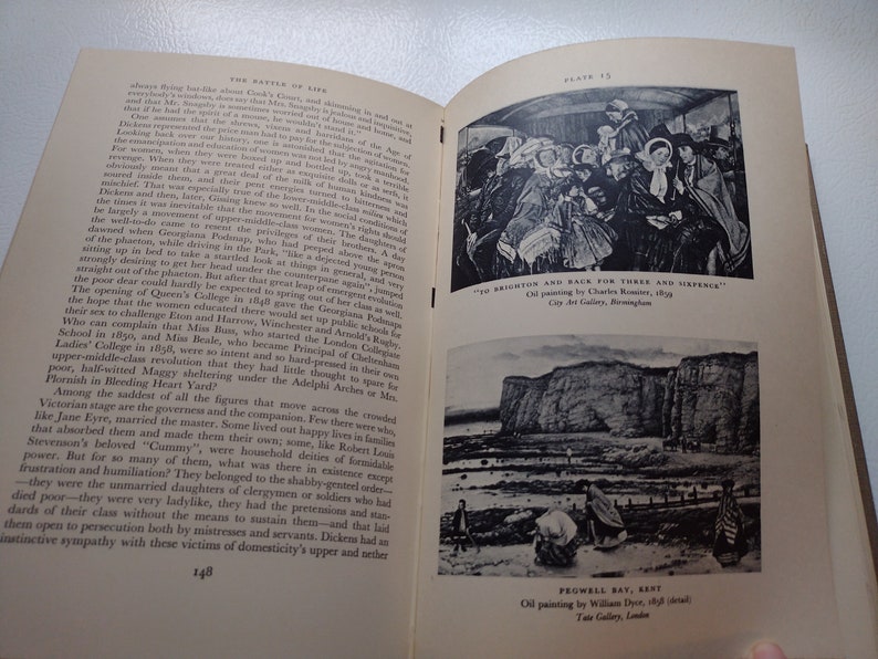 May include: An open book with two black and white illustrations. The top illustration is a painting of people on a bus. The bottom illustration is a painting of a coastal scene. Text on the page includes the title "The Battle of Life".