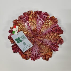 Può includere: Una ciotola decorativa a forma di fiore sbocciato con petali stratificati in tonalità oro metallizzato e magenta intenso. È attaccata un'etichetta bianca con il testo Quadri Foglio Moschini, un codice QR e la frase Hand-painted in Tuscany, Italy.