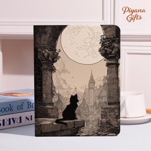 May include: A notebook with a sepia-toned illustration of a black cat silhouetted against a full moon, overlooking a medieval town. The image includes architectural details and the text "Piyana Gifts".