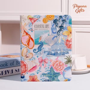 May include: A notebook with a coastal theme. The cover features watercolor illustrations of seashells, seahorses, jellyfish, and sailboats. The text "COASTAL LIFE" is visible on the cover. The notebook is decorated with a variety of colors, including blue, pink, and orange.