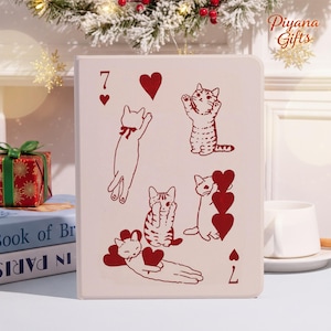 Peut inclure: Un objet décoratif crème avec un motif de carte à jouer orné d'illustrations de chats rouges et de cœurs. La carte affiche le chiffre 7 et le symbole du cœur. L'objet est de forme rectangulaire et est probablement décoratif.
