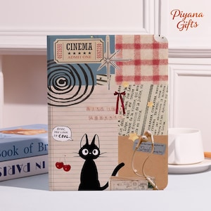 May include: A decorative journal with a collage design. The cover features a black cat illustration, cinema ticket, and text that reads "LIFE IS JOURNEY." The journal has a vintage aesthetic with a red and white checkered pattern.