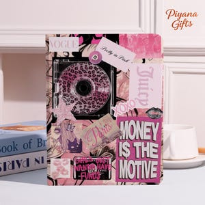 May include: A pink and black notebook with a collage design. The design includes the words "Vogue", "Pretty in Pink", "Juicy", and "Money is the Motive". A CD case with a leopard print design is in the center. A pink star and other stickers are also included.