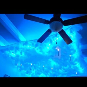 May include: A ceiling fan with a white light fixture and blue LED lights illuminating a cloud-shaped ceiling decoration.