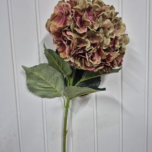 May include: A single stem artificial hydrangea flower with a large, round bloom in shades of green and pink. The flower is made of fabric and has a realistic appearance.