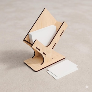 May include: A light-coloured wooden business card holder with a slanted design, featuring dark edges and interlocking joints. The holder contains a stack of blank white rectangular cards, with two additional blank white cards placed flat nearby.
