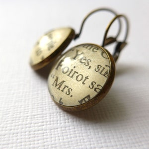 May include: A pair of gold-toned earrings with a round glass charm featuring a vintage book page with the text "Yes, sir, Poirot said "Mrs."
